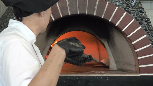Unrecognizable Male Baker turns over Bread in a Wood Burning Stove for Baking. Chef Bakes Flatbread Pita in a Stone Oven