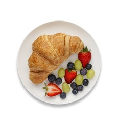 Continental breakfast of a croissant and fruit, shot from above, on white with a drop shadow.