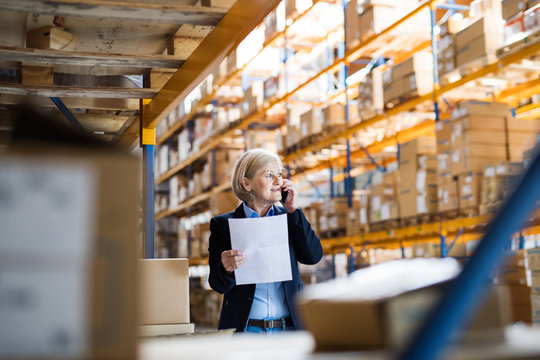 Senior woman warehouse manager or supervisor with smartphone making a phone call.