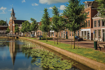 Tree-lined canal with bascule bridge, church, brick houses in street on the banks and sunny day at...