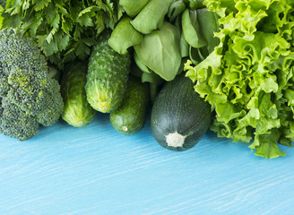 Green vegetables on a blue wooden background. Parsley, spinach, cucumber, broccoli, dill and zucchini. Top view. Green vegetables at border of image with copy space for text.