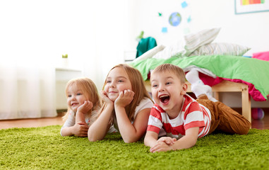 childhood, leisure and family concept - happy little kids lying on floor or carpet