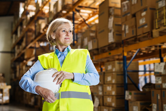 Senior woman warehouse manager or supervisor holding white helmet.
