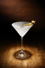 Spotlight on a single chilled martini, with olives, shot on a dark wooden background.