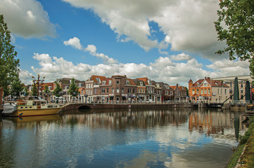 Obraz premium Brick houses, moored boats and bascule bridge reflected in wide canal water surface on sunset in Weesp. Quiet and pleasant village full of canals and green near Amsterdam. Northern Netherlands. 