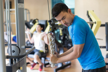 Side view of a young man exhaling while exercising triceps pushdown at the rope cable machine...