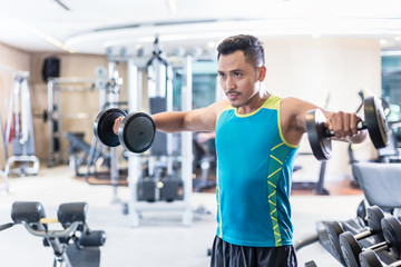 Portrait of a handsome determined young man exercising with dumbbells during upper-body workout routine in a modern fitness club