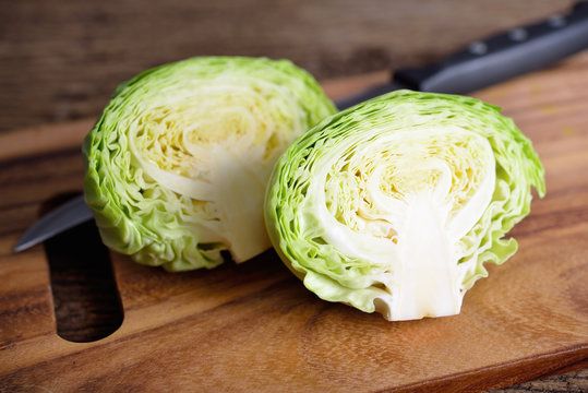 half cut fresh cabbage with knife on wooden cutting board