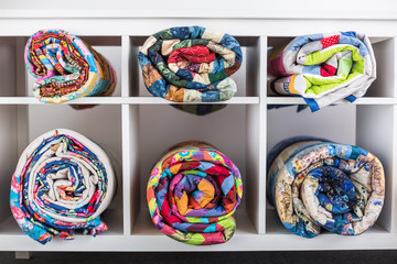patchwork, sewing, tailoring and fashion concept - bright finished quilts in the studio or in the shop, white shelves with six storage compartments for goods, the warehouse of finished products.