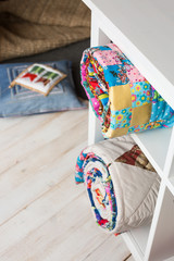 patchwork, sewing and fashion concept - two colorful quilted bedspreads in studio at white shelves with few storage compartments, warehouse of finished products, pillow on floor, top view, vertical.
