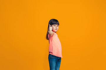 The happy teen girl standing and smiling against orange background.