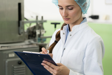 Portrait of a female inspector writing observations about equipment and manufacturing process...