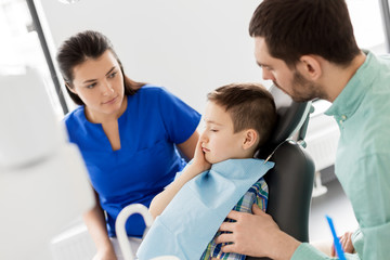 Fototapeta premium medicine, dentistry and healthcare concept - father and son suffering from toothache visiting dentist at dental clinic