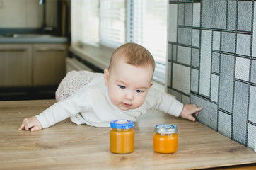 a child on the table in the kitchen next to the jars of mashed pumpkin peach apricot, trying to get...