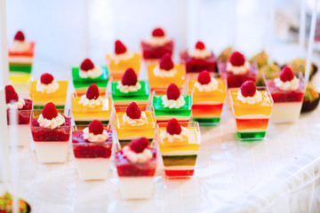 Close-up of a colored jelly with cream and raspberry in transparent cups on a table with a white cloth