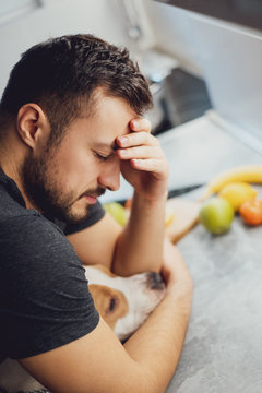 Man hugging his dog while having headache in the kitchen