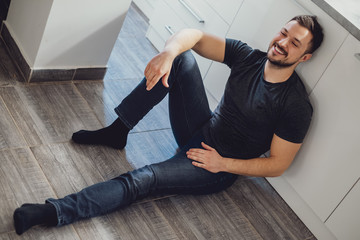 Handsome bearded man smiling while sitting on a kitchen floor