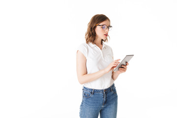 Fototapeta premium Portrait of beautiful lady in eyeglasses standing and thoughtfully working on the tablet on white background isolated