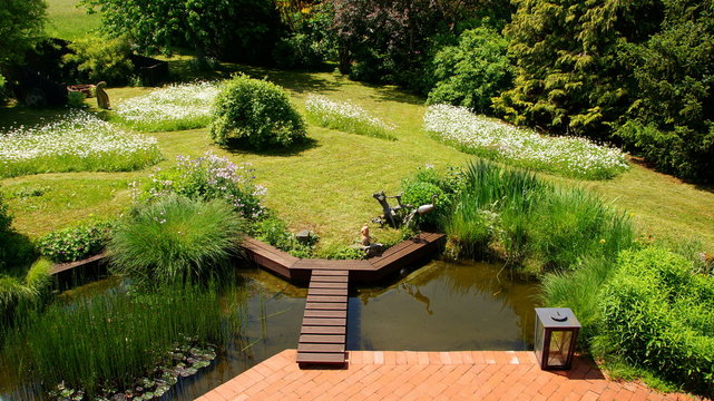 naturbelassener Gartenteich mit Brücke und Margeritenwiese an Terrasse angrenzend