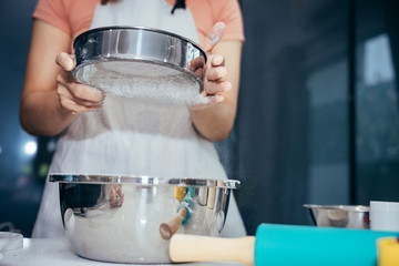 A woman sifting flour into a stainless bowl. Girl is sifting flour to making the bakery in her kitchen on weekend.