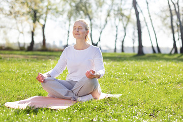 Absolute tranquility. Nice aged woman meditating while sitting in the grass