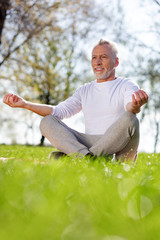 Fototapeta premium Peace of mind. Cheerful aged man sitting in the lotus pose while meditating