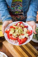 Woman hands holds fresh tomatoes salad with walnuts sauce and onion rings dressing. Spices and herbs, olive oil added. Raw vegan vegetarian healthy food