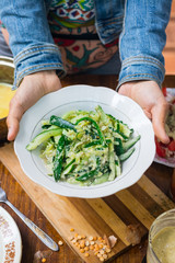 Green cucumber and cabbage salad with walnuts, olive oil and sunflower seeds sauce dressing. Raw vegan vegetarian food. Woman hands holds salad. Lunch or dinner time