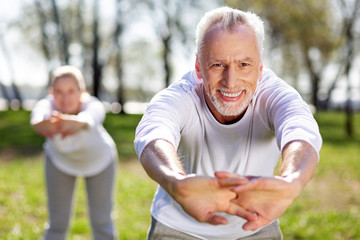 Full of energy. Joyful aged man being in a great mood while doing physical exercises