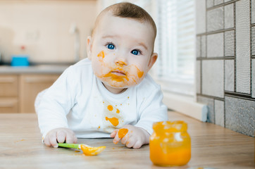 beautiful baby chest all dirty in fruit puree, pumpkin with spoon in hand next to a jar of food