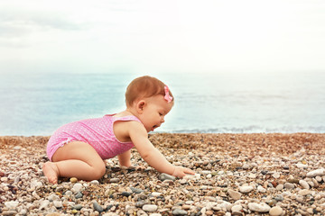 Fototapeta na wymiar little girl in a pink swimsuit playing near the blue sea on a pebble beach