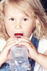 Portrait of a cute little girl in denim overalls, drink water while sitting in studio.