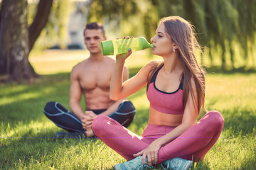 Healthy lifestyle concept. Happy young fitness couple sitting in lotus pose on a green grass.