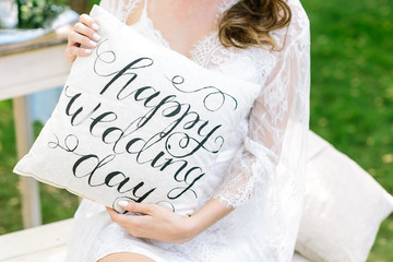decoration, wedding, outdoors concept. young caucasian woman with dark curly hair holding white original pillow with words of congratulation with day of engagement