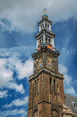 Close-up of pointed bell tower church made of bricks and golden clock under blue sky in Amsterdam. The city is famous for its huge cultural activity, graceful canals and bridges. Northern Netherlands.