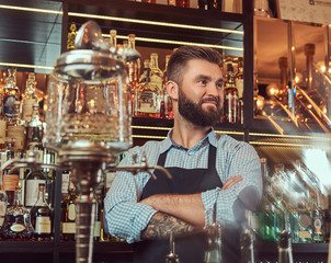 Stylish brutal bartender in a shirt and apron standing with crossed arms at bar counter background.