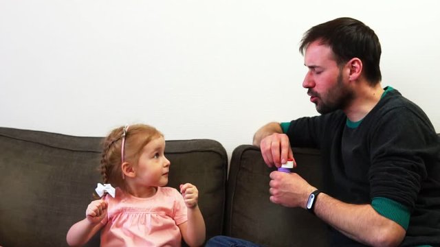 A little girl shows her dad a size of a soap bubble she wishes him to blow