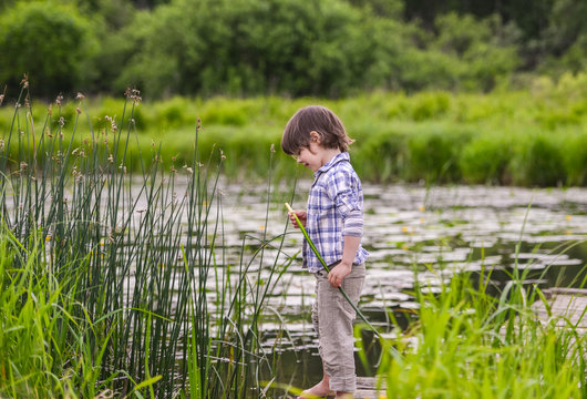 barefoot boy on a wooden bridge on the river. Considering to pull the plant