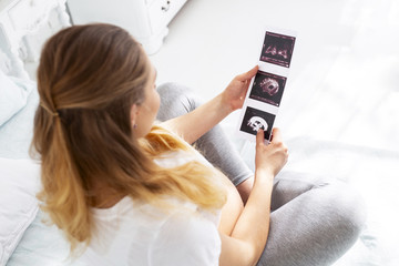 Baby growing. Top view of attractive pregnant woman carrying ultrasound and sitting