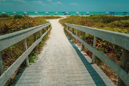 Dramatic horizontal view of a wood bridge looking toward a sandy Sanibel Beach with colorful umbrellas on a sunny day before Hurricane Ian 