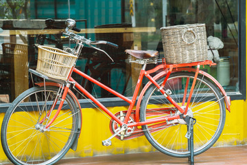 Fototapeta na wymiar Red vintage bicycle with rattan baskets parked near yellow wall container style coffee shop.