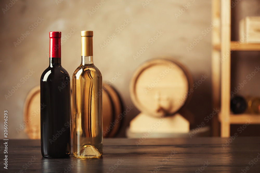 Poster Bottles of delicious wine and blurred barrels on background