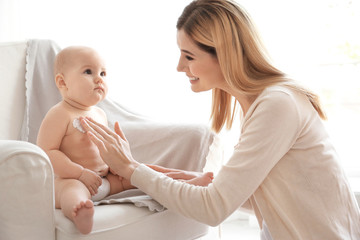 Woman applying body cream on her baby indoors