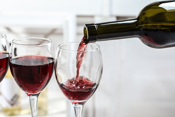 Pouring delicious red wine into glass on light background