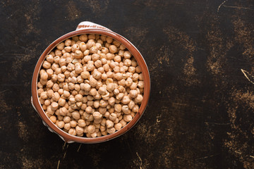 Raw chickpeas in a ceramic bowl on a dark background. A view from above, a copy of space.