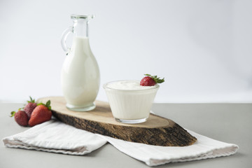 Milk cream cup with strawberry, pitcher of milk on a wooden plate