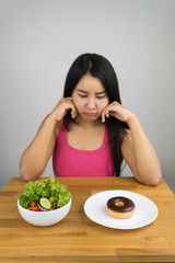 Obraz na płótnie Canvas beautiful plus size Asian woman choosing between salad and chocolate doughnut, dieting concept