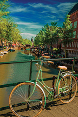 Bridge on canal with bike stuck at balustrade and moored boats under blue sky in Amsterdam. The city is famous for its huge cultural activity and graceful canals. Northern Netherlands. Retouched photo