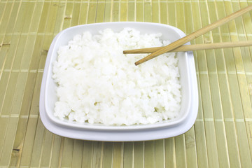 A bowl of cooked white rice with chopsticks on bamboo background