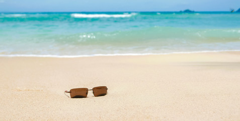 Fototapeta na wymiar Smooth waves and tropical heaven, sunglasses on sand beach